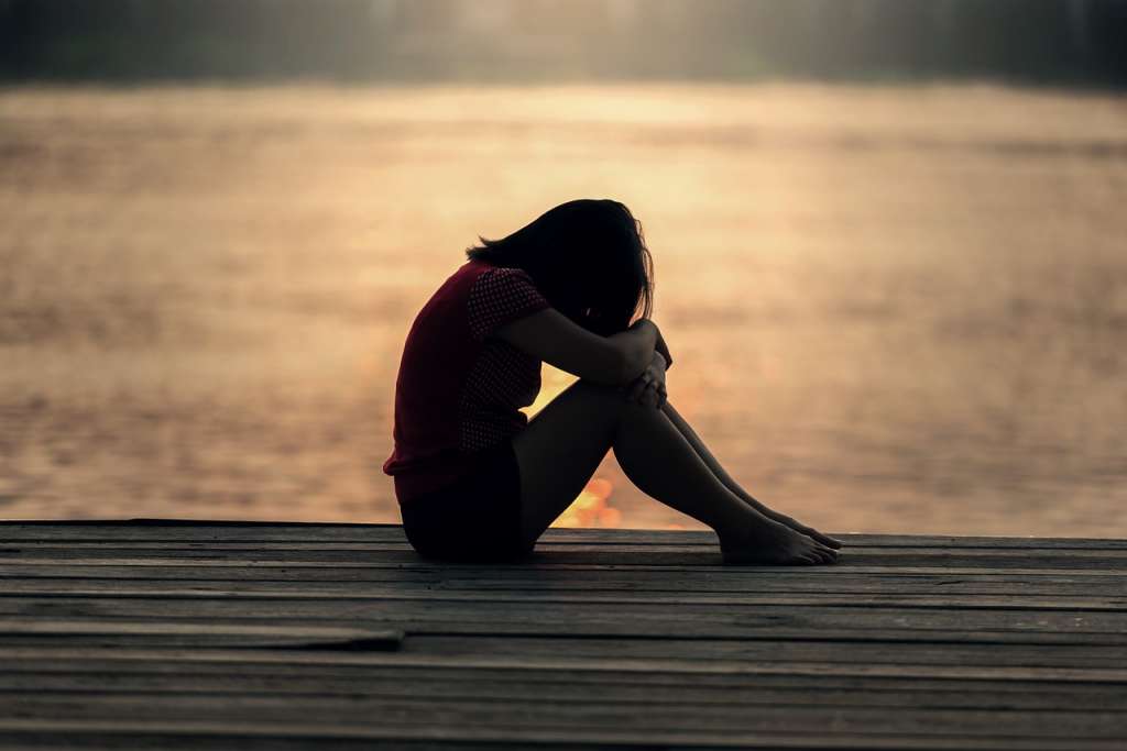 Mujer triste sentada al borde de un lago.