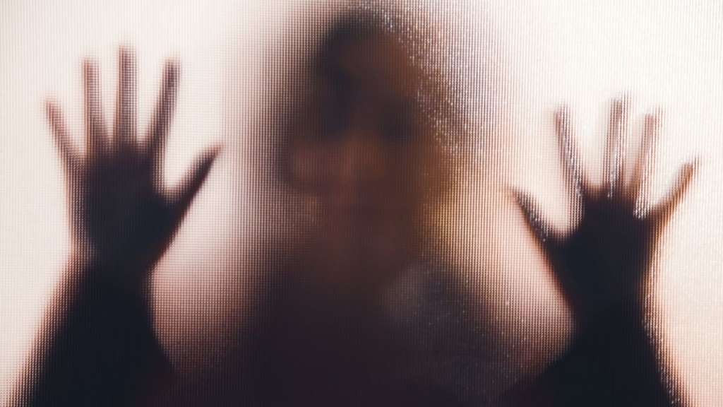 Mujer detras de un cristal semiopaco con las manos apoyadas sobre el.