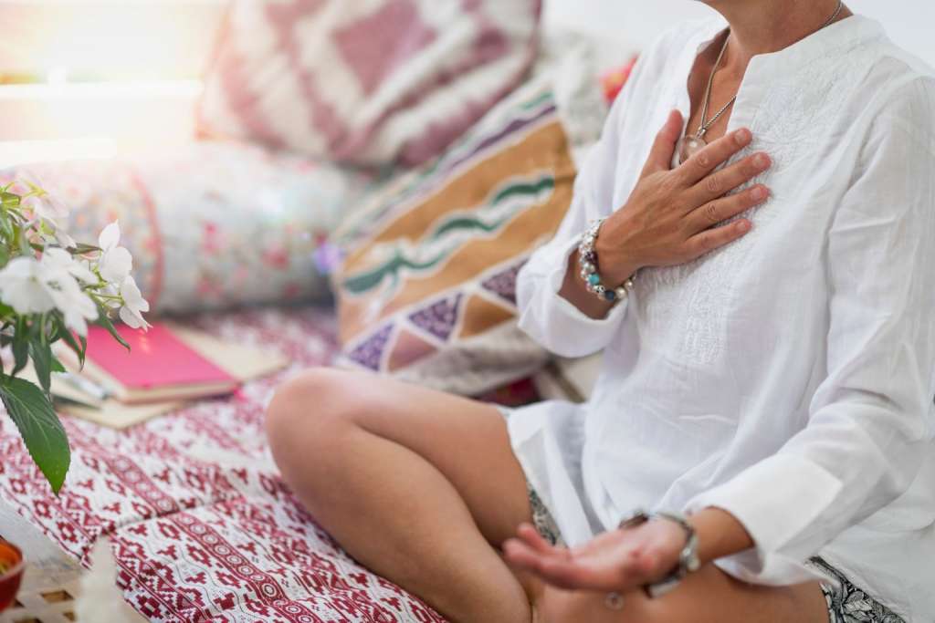 Mujer sentada meditando y con una mano en el corazón practicando el percibir la energía