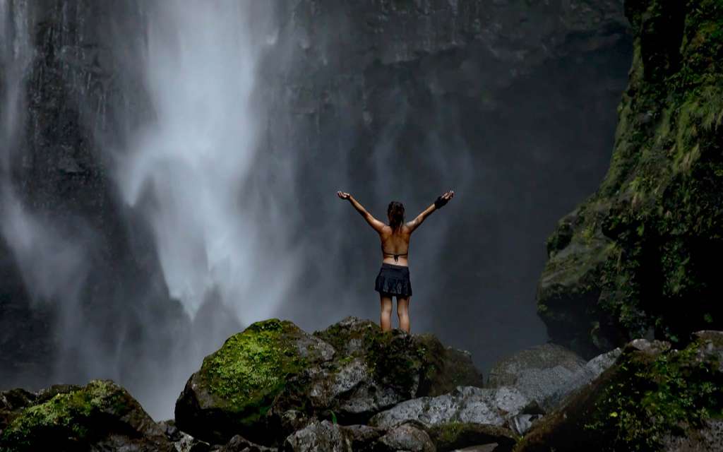 Mujer con los brazos abiertos delante de una cascada